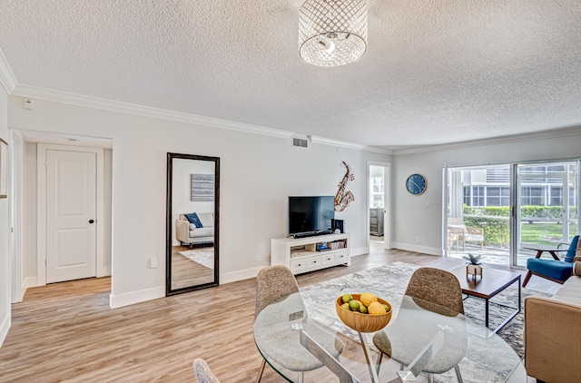 living room with ornamental molding, a textured ceiling, light wood-style floors, and baseboards