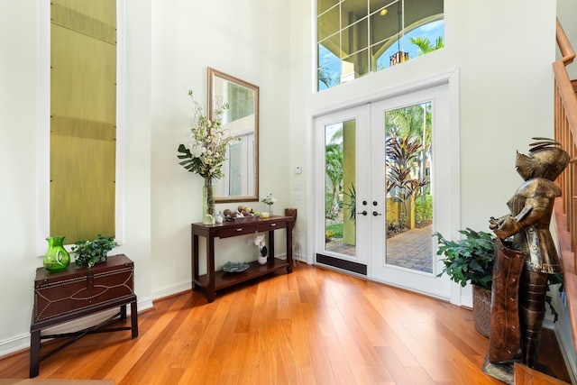 doorway to outside featuring french doors, a towering ceiling, and light hardwood / wood-style floors