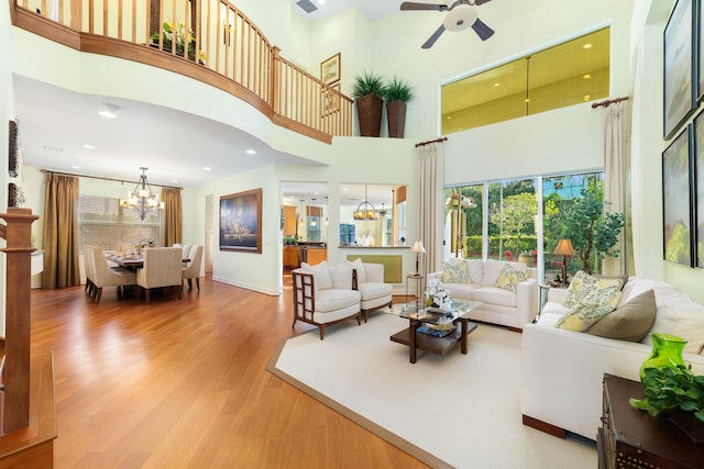 living room with hardwood / wood-style flooring, ceiling fan with notable chandelier, and a high ceiling