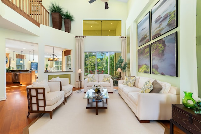 living room with a high ceiling, wood-type flooring, sink, and ceiling fan with notable chandelier