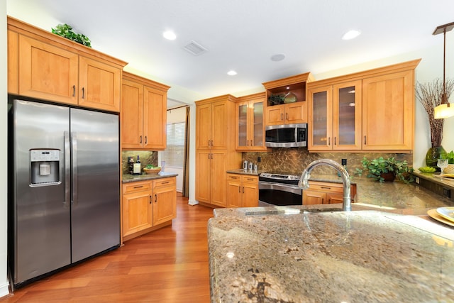 kitchen featuring hanging light fixtures, backsplash, stainless steel appliances, light stone counters, and light hardwood / wood-style floors