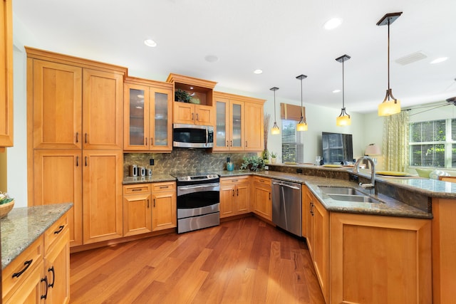 kitchen with appliances with stainless steel finishes, hardwood / wood-style floors, pendant lighting, sink, and backsplash