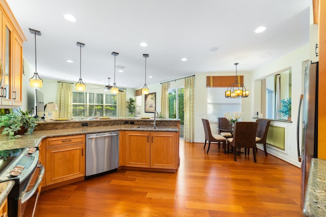 kitchen with sink, appliances with stainless steel finishes, hanging light fixtures, wood-type flooring, and ceiling fan with notable chandelier