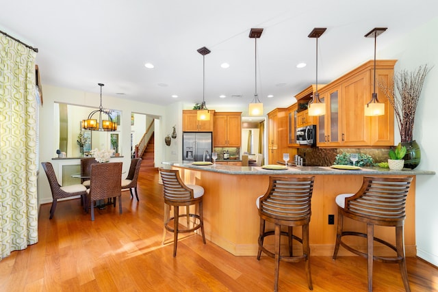 kitchen with tasteful backsplash, light hardwood / wood-style flooring, kitchen peninsula, pendant lighting, and stainless steel appliances