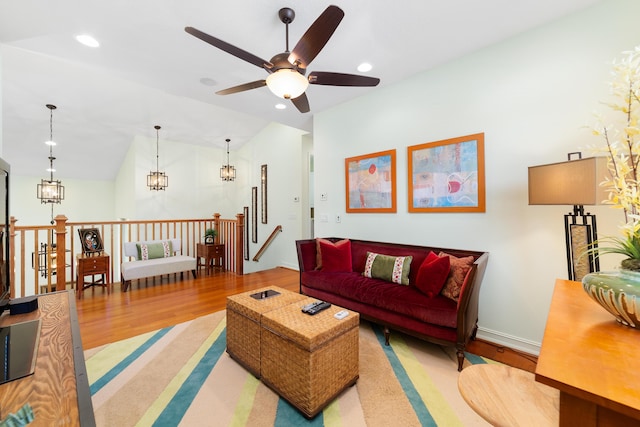 living room featuring vaulted ceiling, ceiling fan with notable chandelier, and hardwood / wood-style floors