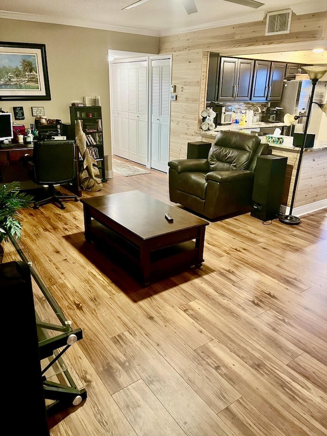 living room with wood walls, crown molding, and light wood-type flooring