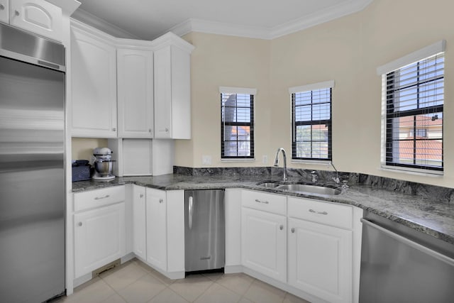 kitchen with crown molding, stainless steel appliances, white cabinetry, a sink, and dark stone counters