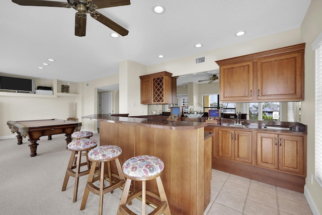 kitchen featuring light tile patterned floors, dark countertops, visible vents, brown cabinetry, and a kitchen breakfast bar