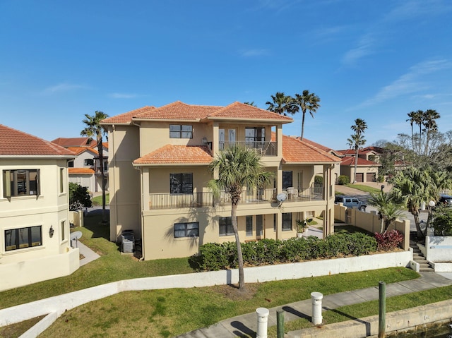 view of front of house with a balcony, central air condition unit, a tiled roof, stucco siding, and a front lawn