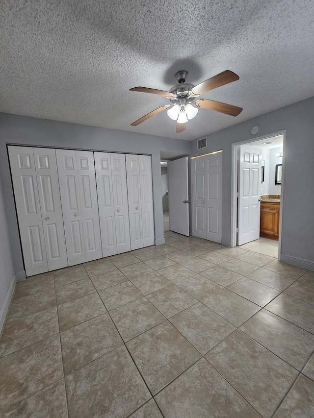 unfurnished bedroom with ensuite bath, ceiling fan, light tile patterned floors, and a textured ceiling