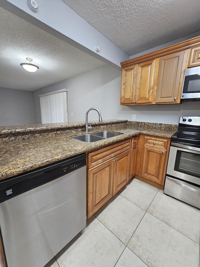 kitchen with sink, dark stone counters, a textured ceiling, light tile patterned floors, and appliances with stainless steel finishes