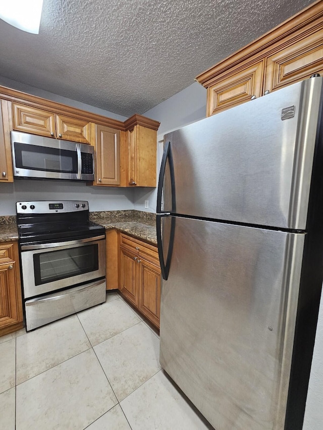 kitchen with light tile patterned floors, a textured ceiling, appliances with stainless steel finishes, and dark stone counters