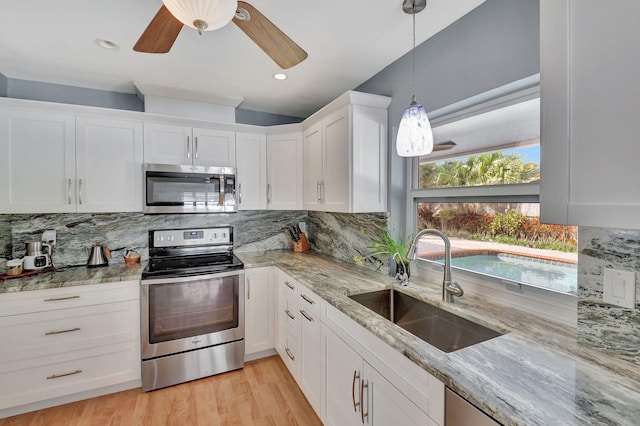 kitchen with appliances with stainless steel finishes, light stone countertops, pendant lighting, white cabinets, and sink