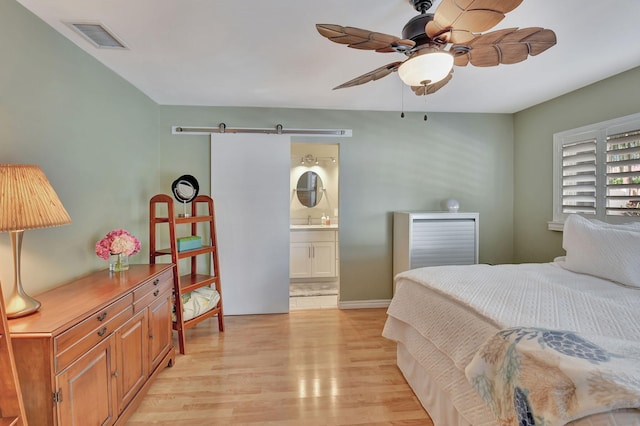 bedroom with sink, ceiling fan, light hardwood / wood-style floors, a barn door, and ensuite bath