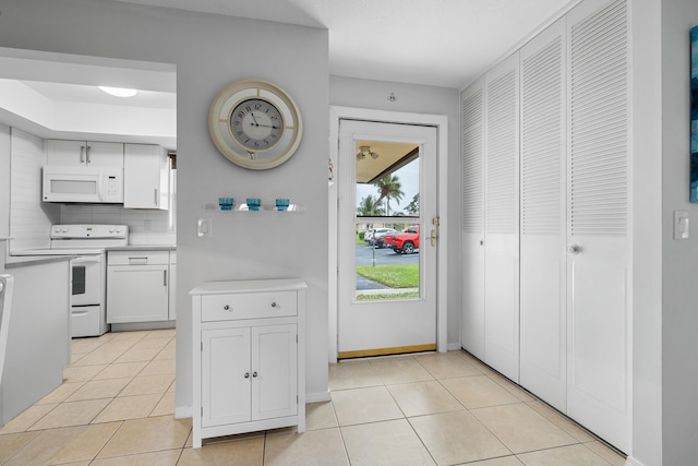 kitchen with white appliances, light tile patterned floors, backsplash, and white cabinetry