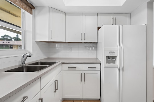 kitchen with sink, white cabinets, backsplash, and white refrigerator with ice dispenser