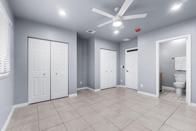 unfurnished bedroom with ceiling fan, light tile patterned floors, connected bathroom, and multiple closets