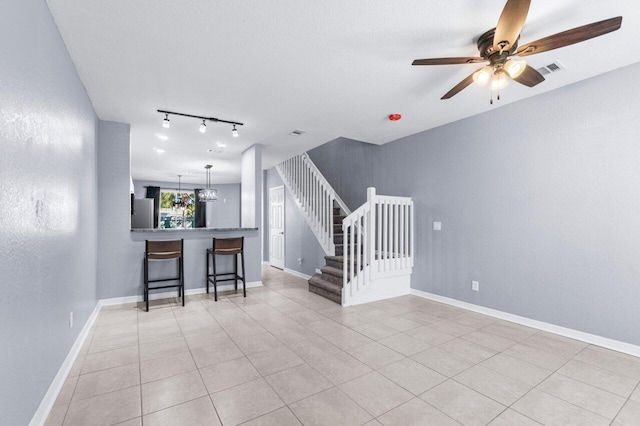 unfurnished living room with ceiling fan with notable chandelier, light tile patterned flooring, a textured ceiling, and track lighting