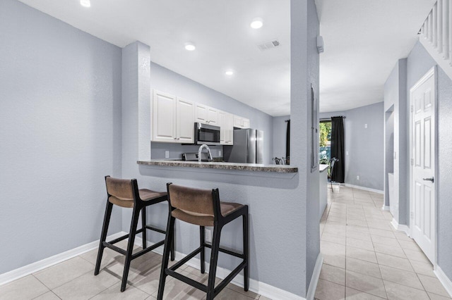 kitchen featuring a breakfast bar, kitchen peninsula, light tile patterned floors, appliances with stainless steel finishes, and white cabinetry