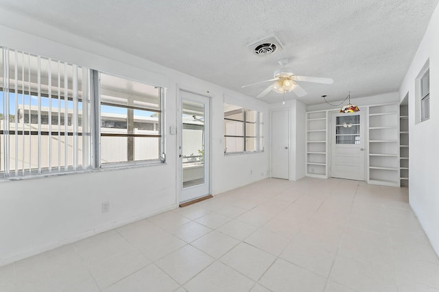 empty room with built in shelves, a textured ceiling, and ceiling fan