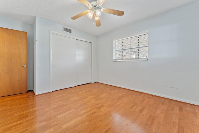 unfurnished bedroom with ceiling fan, a closet, light hardwood / wood-style floors, and a textured ceiling