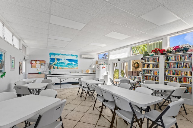 dining area with light tile patterned floors, an AC wall unit, and a drop ceiling