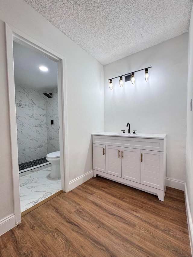 bathroom with vanity, hardwood / wood-style flooring, toilet, a textured ceiling, and a tile shower