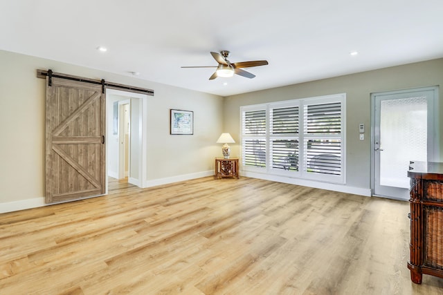 unfurnished living room featuring a barn door, light hardwood / wood-style floors, and ceiling fan