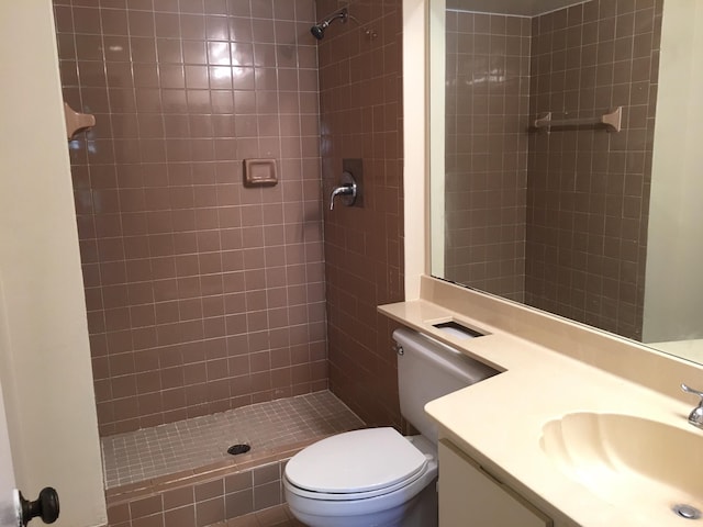 bathroom featuring a tile shower, vanity, and toilet