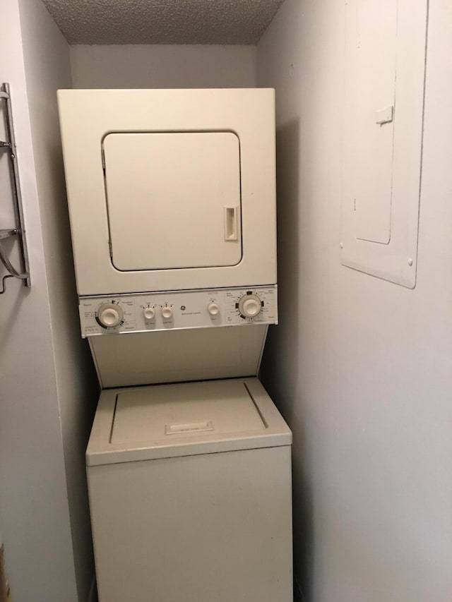 washroom featuring a textured ceiling, electric panel, and stacked washer and clothes dryer