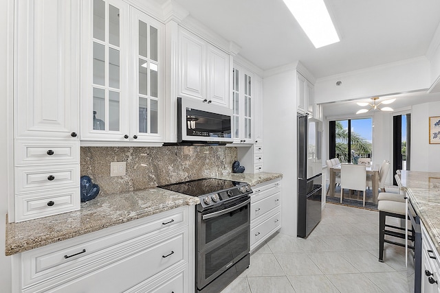 kitchen featuring appliances with stainless steel finishes, light stone counters, white cabinets, an inviting chandelier, and backsplash