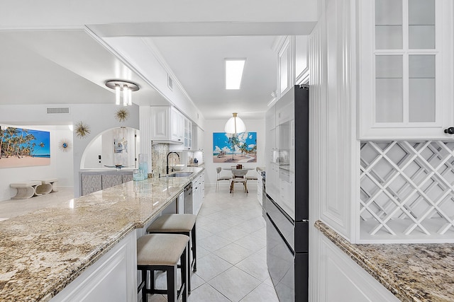 kitchen with light stone counters, white cabinets, light tile patterned flooring, a kitchen breakfast bar, and sink