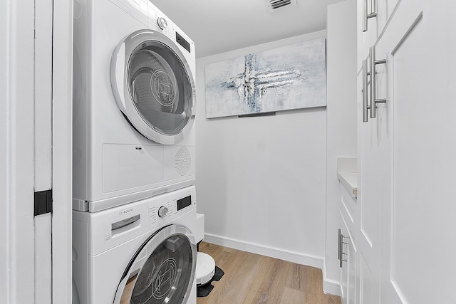 laundry area with stacked washer and dryer and light hardwood / wood-style floors