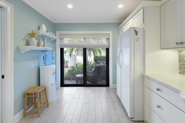 interior space featuring light hardwood / wood-style flooring, white cabinetry, white fridge with ice dispenser, and ornamental molding