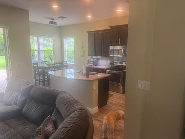 kitchen with dark brown cabinetry, stainless steel appliances, sink, hardwood / wood-style flooring, and a center island with sink