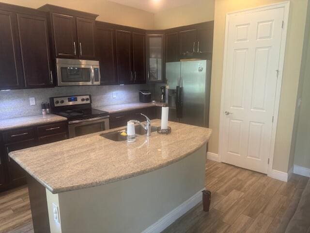 kitchen with light stone countertops, sink, hardwood / wood-style floors, a kitchen island with sink, and appliances with stainless steel finishes