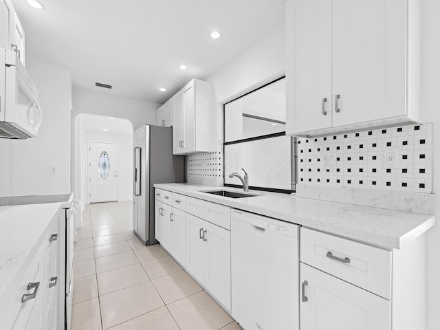 kitchen with white appliances, light stone counters, white cabinets, light tile patterned flooring, and sink