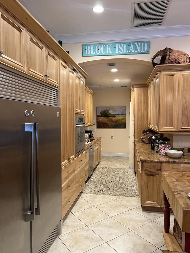 kitchen with light tile patterned floors, ornamental molding, stainless steel appliances, and stone countertops