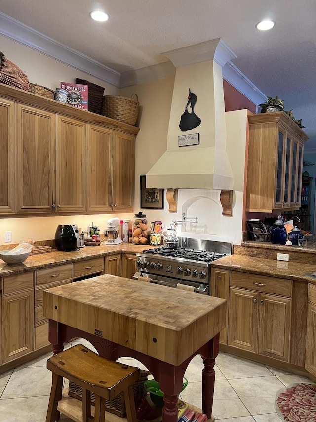 kitchen featuring premium range hood, light tile patterned flooring, high end stove, dark stone counters, and ornamental molding