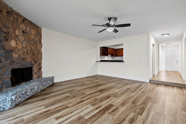 unfurnished living room with sink, a fireplace, ceiling fan, and hardwood / wood-style flooring