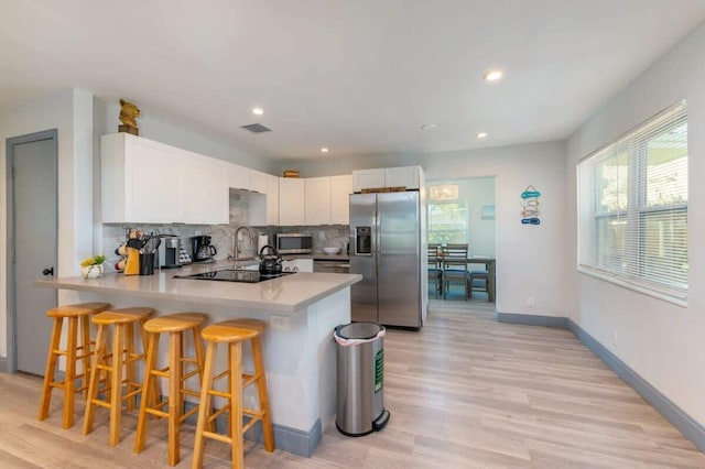 kitchen featuring kitchen peninsula, appliances with stainless steel finishes, a breakfast bar area, white cabinets, and light wood-type flooring