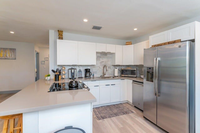 kitchen with kitchen peninsula, a kitchen bar, stainless steel appliances, sink, and white cabinetry