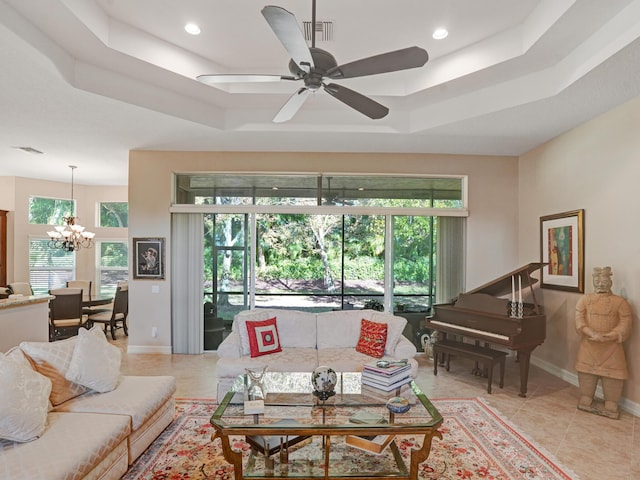 living room with ceiling fan with notable chandelier, a raised ceiling, and light tile patterned flooring