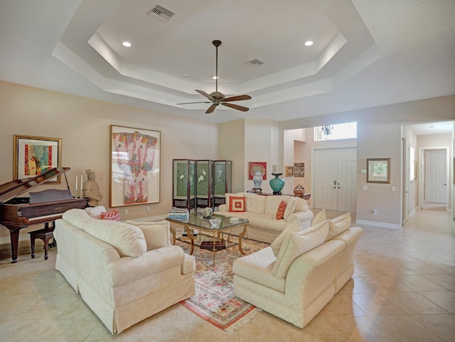 living room with a tray ceiling, ceiling fan, and light tile patterned flooring