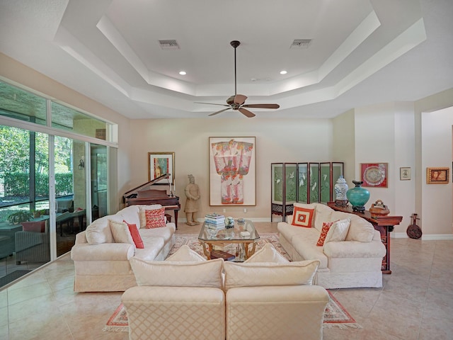 living room featuring ceiling fan, light tile patterned flooring, and a tray ceiling