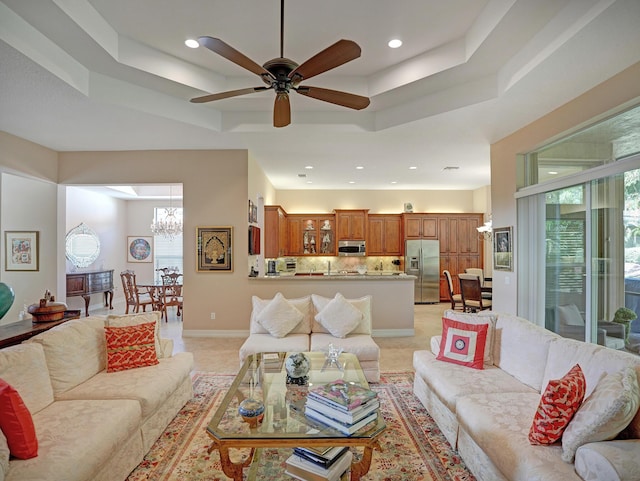 living room with ceiling fan with notable chandelier and a tray ceiling