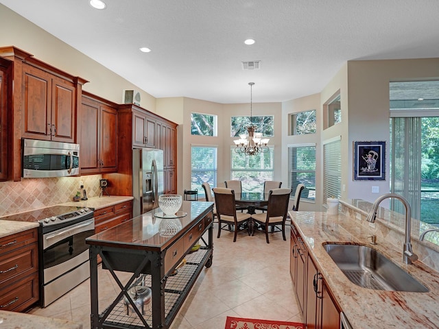 kitchen featuring sink, stainless steel appliances, an inviting chandelier, light stone counters, and pendant lighting