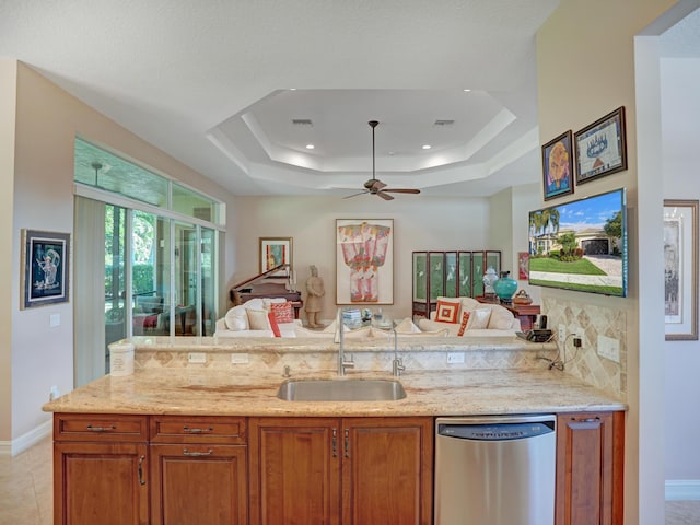 kitchen featuring a raised ceiling, sink, stainless steel dishwasher, ceiling fan, and light stone countertops