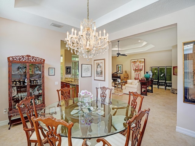 tiled dining space with a tray ceiling, sink, and ceiling fan with notable chandelier