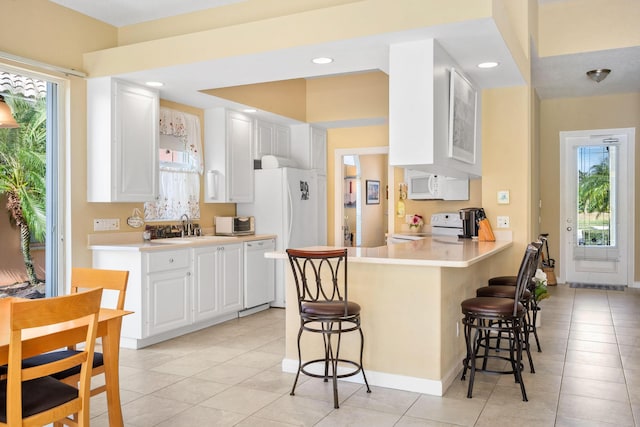 kitchen featuring a breakfast bar area, kitchen peninsula, white cabinetry, and white appliances